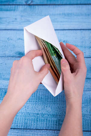 Hands holding an open envelope with money on a blue backgroundの写真素材