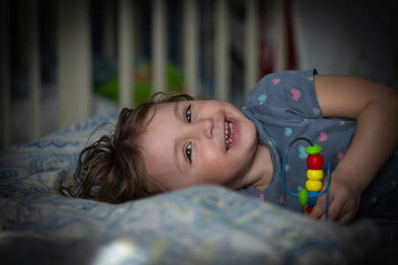 A little girl lies on the bed with a toy and smiles close-upの写真素材