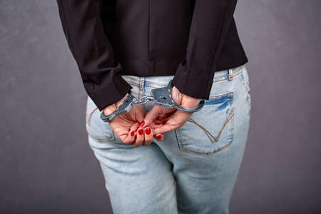 women's handcuffed hands hold dollars on a dark wooden backgroundの写真素材