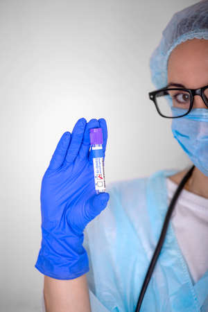 A blonde girl with glasses, a medical worker, shows a test tube with a positive test result for covid. Focus on the test tube.の写真素材