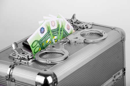 Handcuffs lying on a briefcase with money sticking out of it