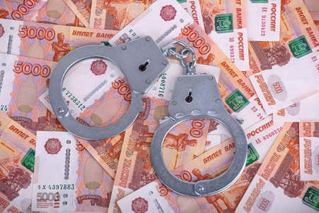 Handcuffed hands hold an open envelope with euro bills, on a dark wooden background