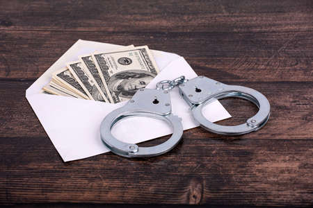 Handcuffed hands hold an open envelope with euro bills, on a dark wooden backgroundの写真素材
