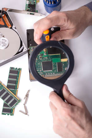 The master examines the disassembled hard drive through a magnifying glass on the desktop next to...