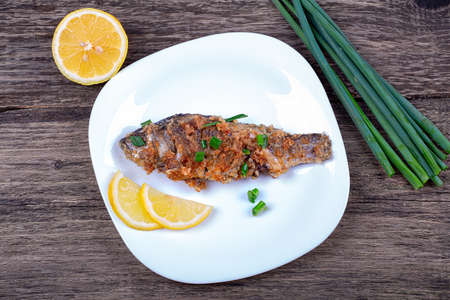 Fried breaded fish with green onions and lemon, in a plate on an old wooden backgroundの写真素材