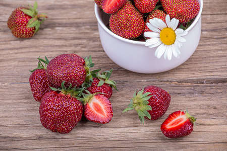 Large ripe strawberries, whole and in pieces, in a plate and lying separately on a wooden background, close-upの写真素材