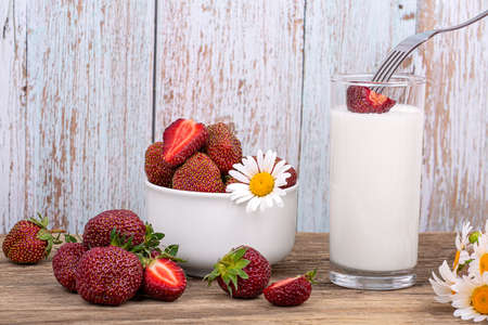 Ripe strawberries on a fork are dipped in a glass of milk, a plate with strawberries on a wooden background, close-upの写真素材