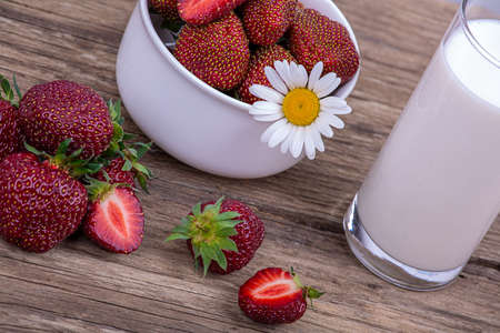 A glass of fresh milk and a plate of ripe red strawberries on a wooden background, close-upの写真素材