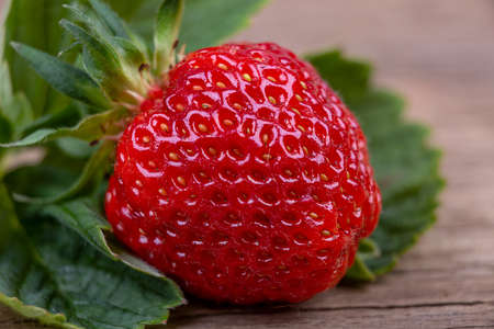 Ripe strawberry with leaves on a wooden background, macro photographyの写真素材