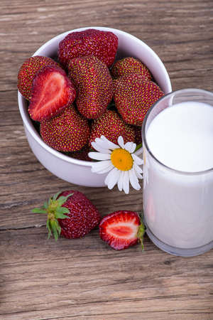 A glass of fresh milk and a plate of ripe red strawberries on a wooden background, close-upの写真素材