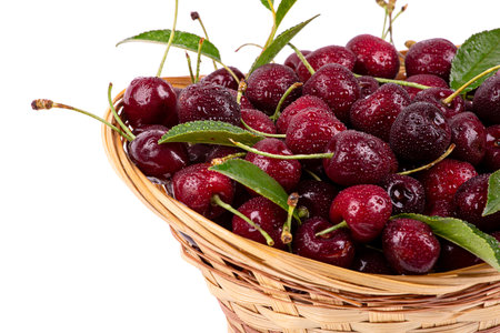 Ripe cherry in drops of water, in a wicker basket, isolated on a white background, close-upの写真素材