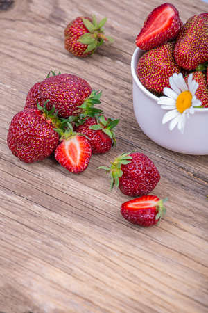 Large ripe strawberries, whole and in pieces, in a plate and lying separately on a wooden background, close-upの写真素材