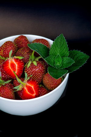 Large ripe strawberries with a fresh sprig of mint, on a black background, close-upの写真素材