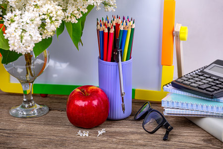 I'm going to school soon. A stack of books, notebooks, a calculator, an apple, glasses and a branch of white lilac on a wooden backgroundの写真素材
