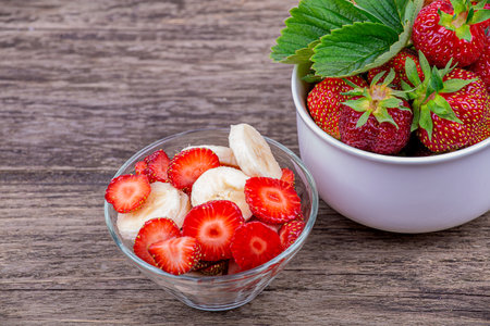 Fresh strawberries, a plate with sliced strawberries and a banana, on a wooden backgroundの写真素材