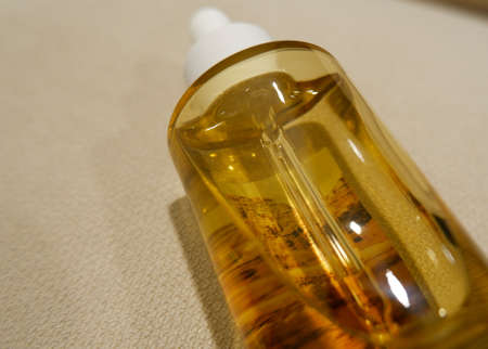 A golden glass ampoule bottle lying on a beige sofa, closed upの写真素材
