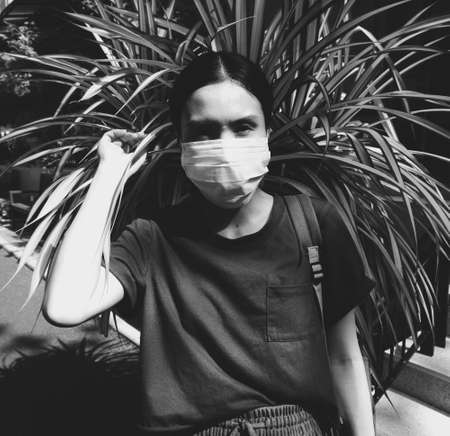 Black and white portrait of an Asian woman wearing a facial mask against strong sunlightの写真素材