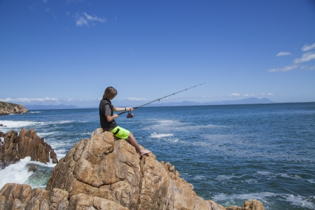 young teenage boy fishing by the sea on some rocks