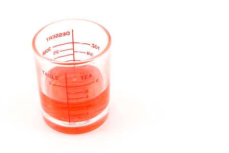 Red syrup in syrup measuring glass on white background.の写真素材