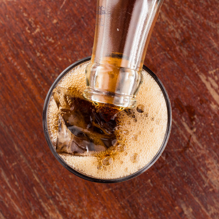 Pouring cola into the glass on wooden table.