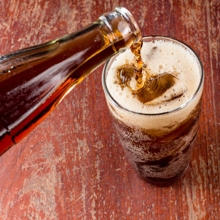 Pouring cola into the glass on wooden table.