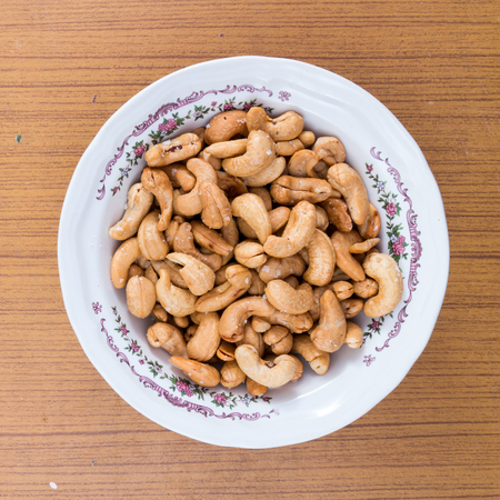 salted and roasted peanuts in white bowl on wooden table.の写真素材