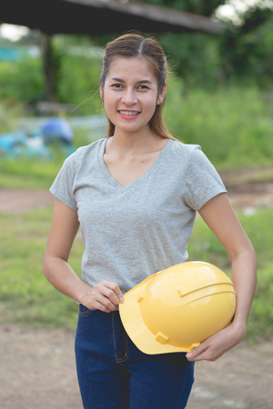 Female workers dressed in gray t-shirt and jeans holding a yellow helmetの写真素材