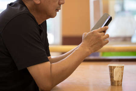 Man reading news in smart phone with a paper cup of coffee in coffee shop.