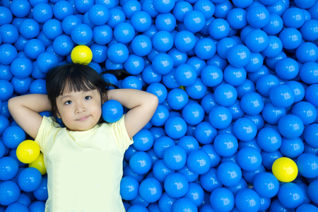 Little asian girl playing lying in colorful balls park playground.の写真素材