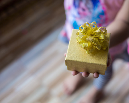 Close up of kid holding a little gold gift box in a gesture of giving with copy space.
