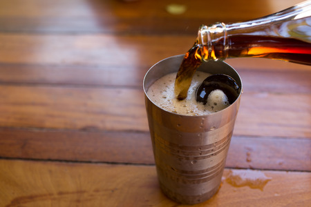 Pouring cola into the glass with ice on wooden table