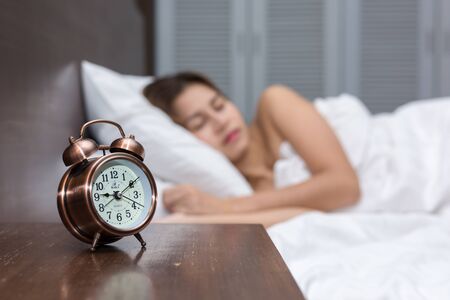 Close up of alarm clock on table and woman sleeping in background.の写真素材