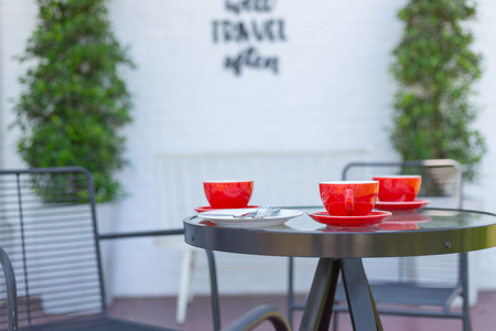 Red coffee mug placed on a table in a coffee shop with white brick wall background.の写真素材