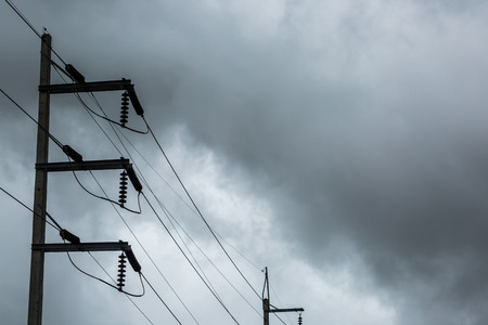 Electricity pole and high voltage power lines on the road with cloud and overcast sky.の写真素材