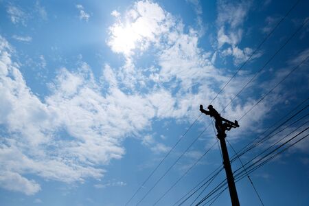 Silhouetted electricians working at electric pole in blue sky background