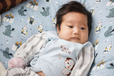 Asian infant lying on a bed.