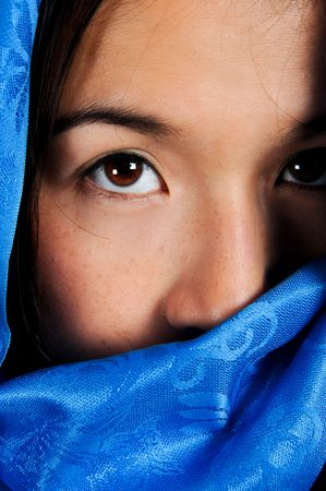 Asian woman behind blue fabric looks at camera