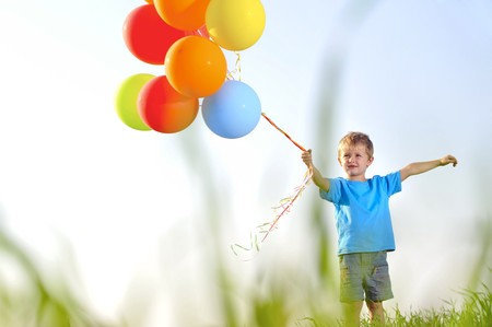 Young boy playing with a bunch of balloons outside, shot through grass in the fieldの写真素材