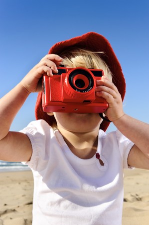 Adorable little girl takes pictures with her red camera on the beachの写真素材