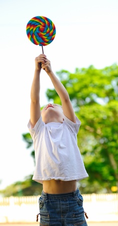 Young boy holds his lollipop high above his headの写真素材