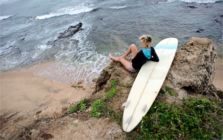 Female surfer sitting on cliffside with surfboardの写真素材