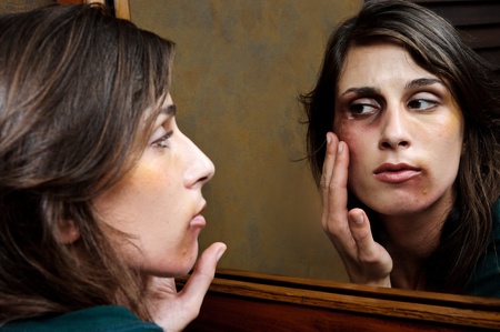 Battered woman checks the extent of her injuries in the bathroom mirrorの写真素材