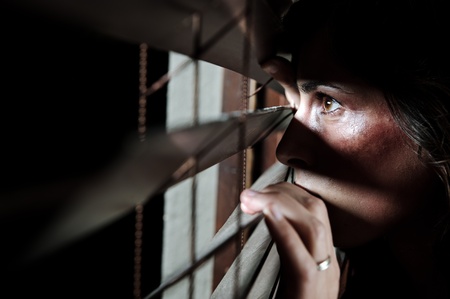 Fearful battered woman peeking through the blinds to see if her husband is homeの写真素材