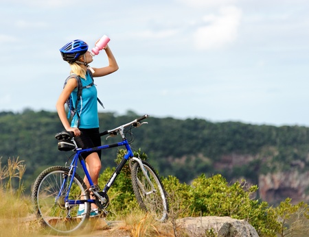 Attractive, healthy woman drinks from her water bottle on mountain bike. active outdoor lifestyle concept の写真素材