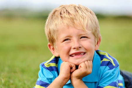 A blond child lies on some grass on a summer day 