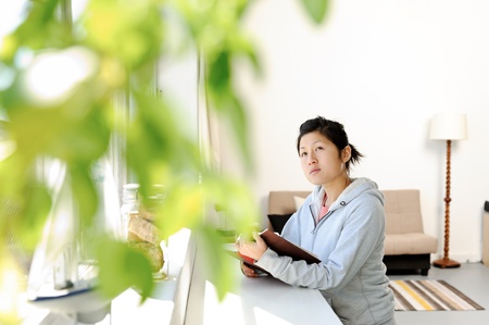 Young asian girl looks up from her book and looks out the window