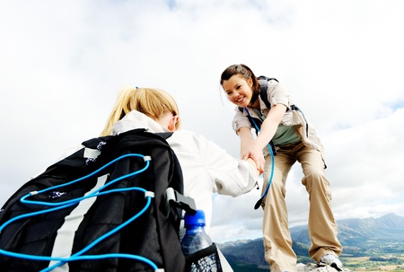 Hiking woman helps her friend climb onto the rock, outdoor lifestyle concept