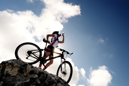 Cyclist drinks water on top of a mountain with bike on a sunny day