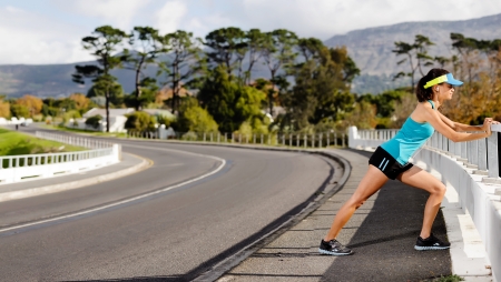 Panorama of fitness woman stretching her calf muscle on a bridge after a long endurance marathon...
