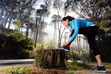 runner tying her shoelace while preparing for fitnes training outdoors in the forest with morning sinlightの写真素材
